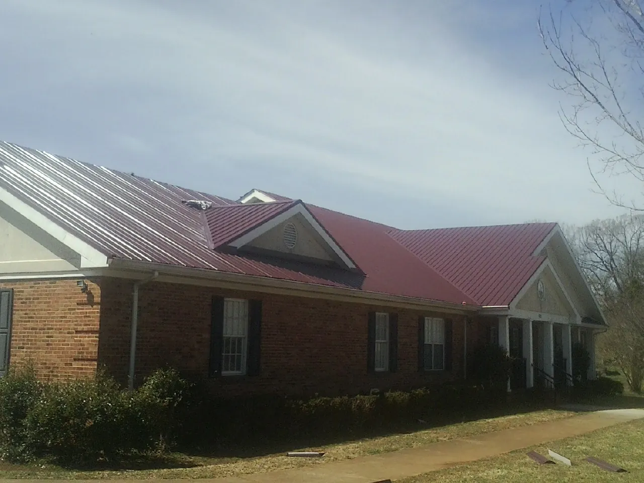 Red metal roof with gabled entries on a long brick building, from a Hail Damage Roof Repair job in Orange